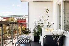a Nordic balcony with a black floor, black furniture with printed and neutral upholstery, potted blooms and candle lanterns