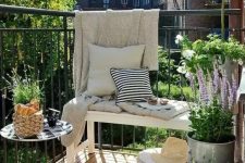 a Nordic summer balcony with a white bench, a metal table, potted greenery and blooms, neutral and printed textiles