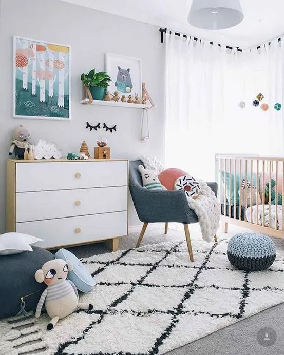 a Scandi nursery with bright touches   artworks, pillows, a pouf and a chair and some bright bedding in the crib is lovely