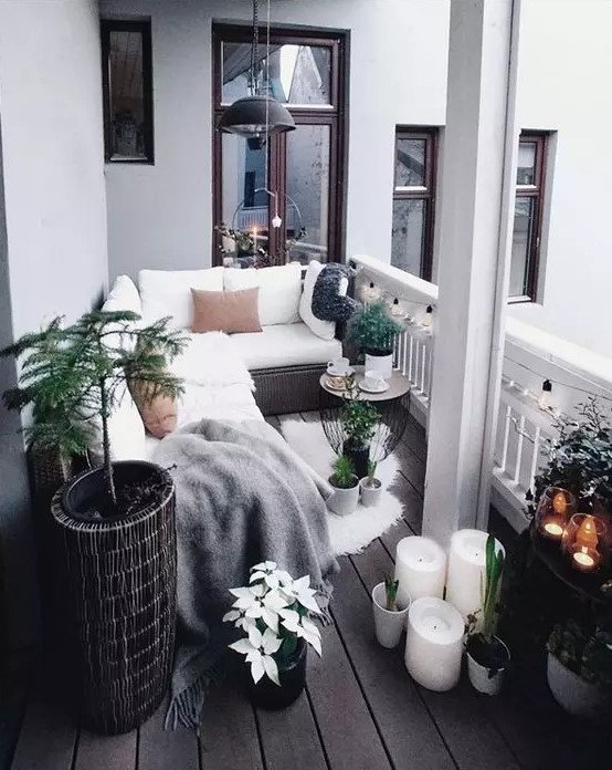 a Scandinavian balcony with a wicker corner sofa with white upholstery, candles and potted plants, some blooms and pendant lamps