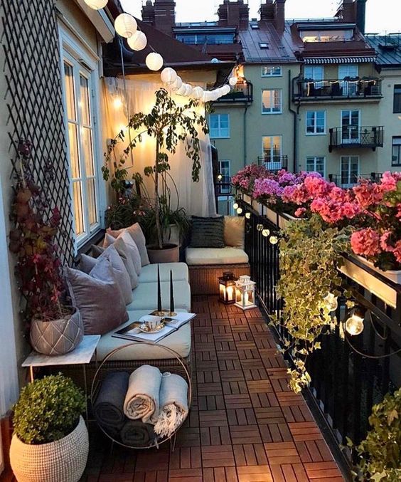a Scandinavian balcony with greenery and blooms, wicker seating furniture, lights and candle lanterns is welcoming and chic