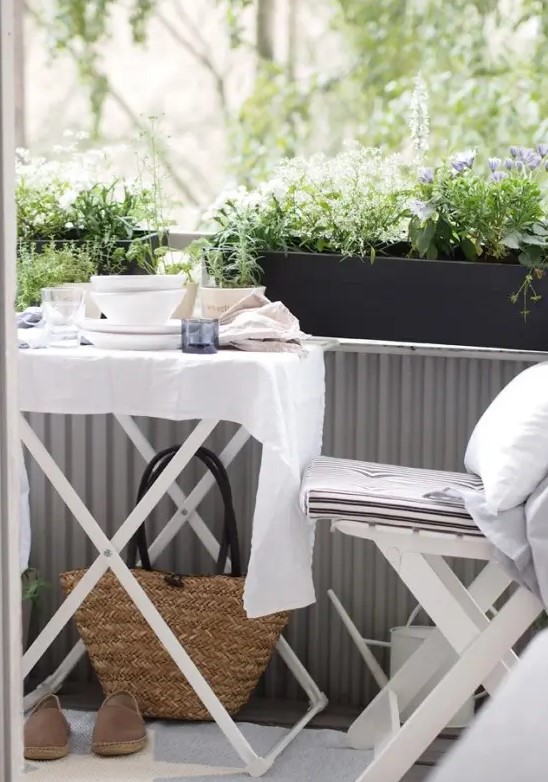 a Scandinavian balcony with white folding garden furniture, black planters with greenery and blooms and white textiles is a lovely idea