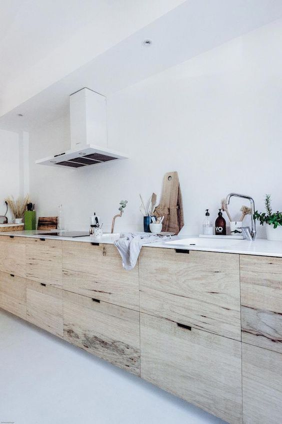 a Scandinavian kitchen with stained sleek cabinets, white stone countertops, a white hood and metallic touches is cool