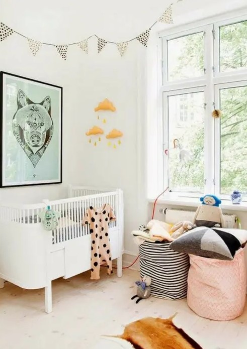 a Scandinavian nursery with a white crib, a green artwork, printed bunting, printed baskets with pillows and toys and a mobile