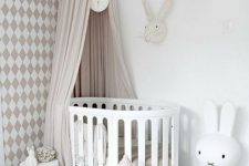a beautiful neutral nursery with a geo printed wall, a white crib and a play crib, a Miffy lamp and a play rug