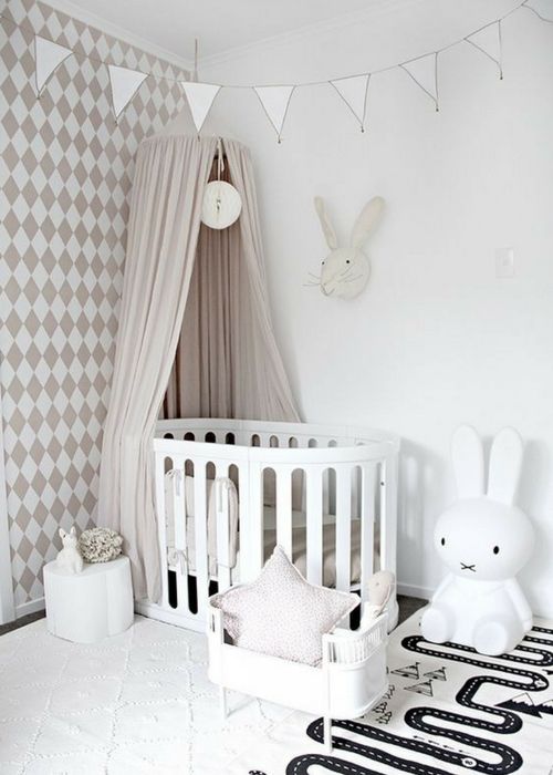 a beautiful neutral nursery with a geo printed wall, a white crib and a play crib, a Miffy lamp and a play rug