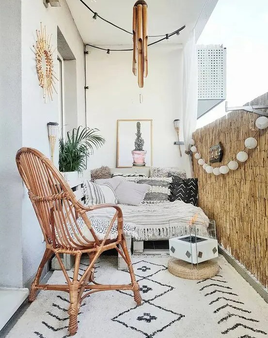 a black and white boho balcony with a low sofa with boho upholstery, bamboo, a rattan chair, a printed rug and even a portable fireplace