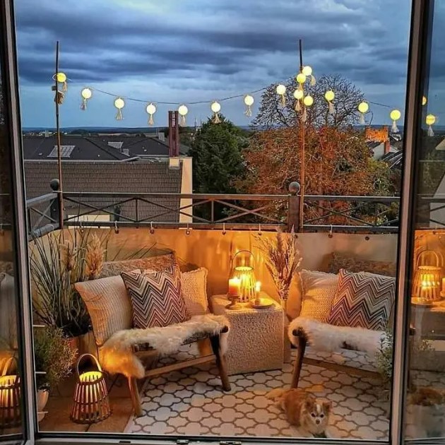 a boho balcony with a printed rug, neutral chairs with printed boho pillows, candle lanterns, potted plants and pampas grass in vases
