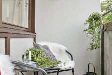 a bright Scandinavian balcony with black metal furniture, bright textiles and faux fur, potted plants and greenery