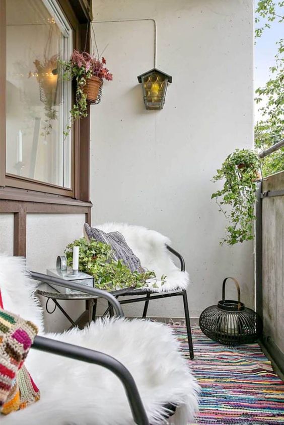 a bright Scandinavian balcony with black metal furniture, bright textiles and faux fur, potted plants and greenery