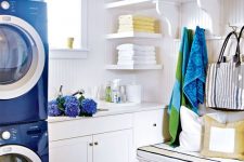 a bright laundry with sleek white cabinets, open shelves, a striped rug and navy appliances bold blue and green towels