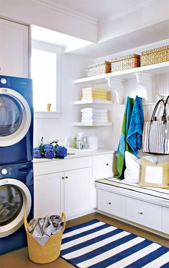 a bright laundry with sleek white cabinets, open shelves, a striped rug and navy appliances bold blue and green towels