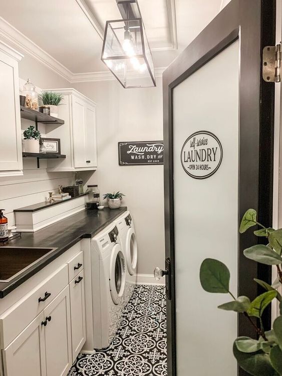 a chic black and white laundry room with a white shiplap wall, white shaker cabinets, black and white floor tiles and potted greenery