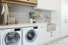 a chic laundry with a grey tile backsplash, a bold tiled floor, white cabinets and an open shelf is welcoming and functional