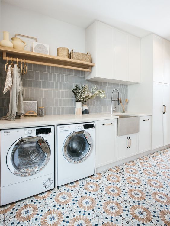 a chic laundry with a grey tile backsplash, a bold tiled floor, white cabinets and an open shelf is welcoming and functional