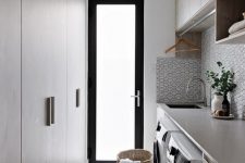a chic minimalist laundry with sleek wooden cabinets, a black and white tile backsplash, a washing machine and a dryer and a basket for laundry