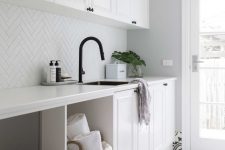 a chic modern laundry done in white, with shaker style cabinets, a black and white printed tile floor, a black faucet and a sink