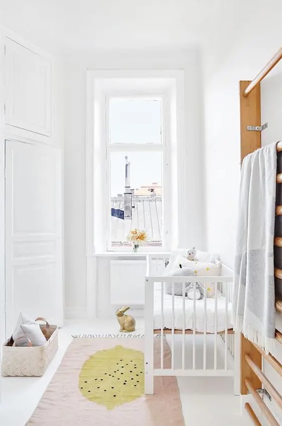 a chic neutral Scandi nursery with white furniture, pastel pillows and a rug, a basket for storage is a small and cute space