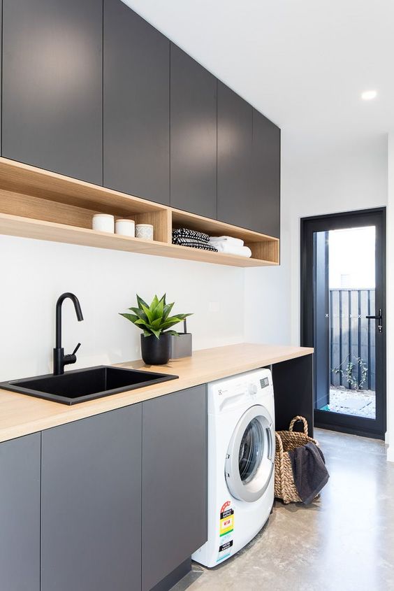 a clean and sleek graphite grey laundry with sleek cabinets, stained countertps and box shelves, a black frame glass door