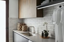 a contemporary laundry with sleek stained cabinets, a concrete countertop, neutral narrow tiles on the backsplash and a neutral floor