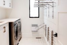 a contemporary white laundry with sleek cabinets and metal handles, a black washing machine and a dryer, metal wall-mounted shelves