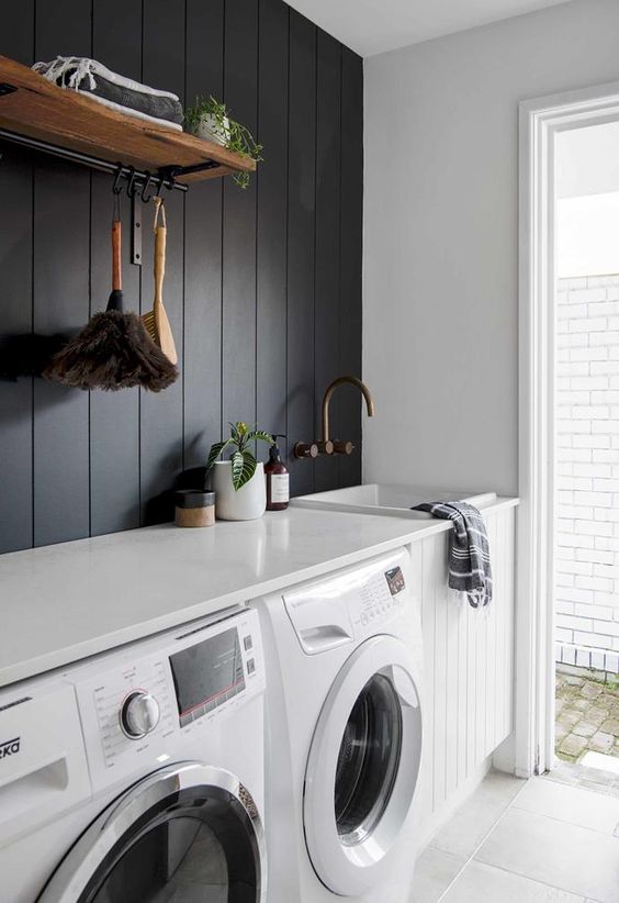 a contrasting laundry with a black shiplap wall, a white shiplap cabinet, white appliances and a countertop plus a door to the garden