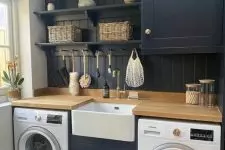 a cool black laundry with shaker cabinets, a shiplap wall, a stained countertop, baskets and potted plants and blooms