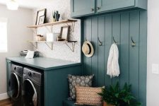 a cool blue farmhouse laundry with a storage unit, black appliances, open shelves and printed wallpaper and a potted plant