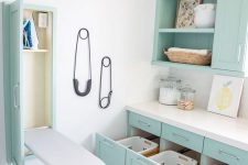 a cool turquoise laundry room with shaker cabinets, a white stone countertops, a hidden ironing board and drawers for laundry