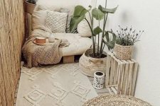 a cute boho balcony done in creamy shades, with a low seat with boho pillows, a beautiful rug, a crate and a basket with a plant, a jute pouf and some candle lanterns
