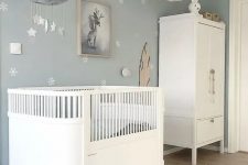 a dreamy Scandi nursery with pale blue walls and an accent one, white furniture, pendant lamps and a mobile plus toys