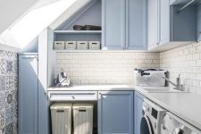 a dusty blue laundry with shaker style cabinets, a white subway tile backsplash, a bold blue and white printed tile floor and neutral appliances