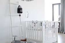 a grey and white Scandinavian nursery with a white crib and neutral bedding, grey curtains, a vintage play car, a black banner and black and white pompoms