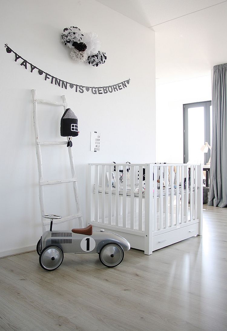 a grey and white Scandinavian nursery with a white crib and neutral bedding, grey curtains, a vintage play car, a black banner and black and white pompoms