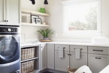 a grey farmhouse laundry with shaker style cabinets, a tiled floor, open shelving, navy appliances and baskets for storage