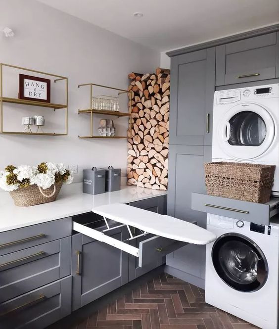 a grey laundry room with shaker style cabinets, white stone countertops, firewood storage and appliances
