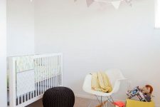 a lovely Nordic nursery with a white crib and a white chair, layered rugs, pretty toys and pillows and pastel bedding