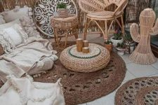 a lovely boho balcony with jute rugs, rattan furniture, a low sofa with lots of pillows, a pouf, a jute pouf with candles and potted plants