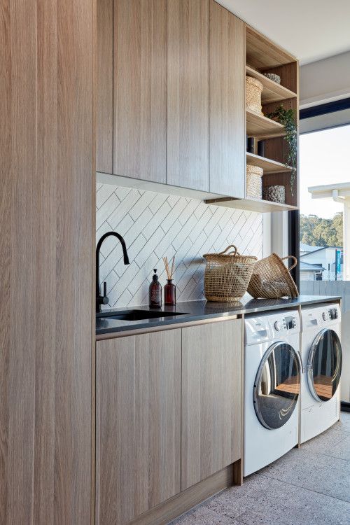 a lovely mid century modern laundry with sleek stained cabinetry, a diagonal white tile backsplash, a black counertop and fixtures