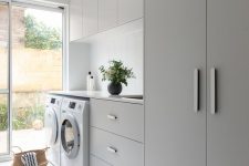 a lovely minimalist laundry with sleek grey cabinets and a wardrobe, a white skinny tile backsplash and neutral appliances is cool