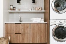 a mid-century modern laundry with sleek stained cabinets, a grey skinny tile backsplash, a jute rug and stacked appliances