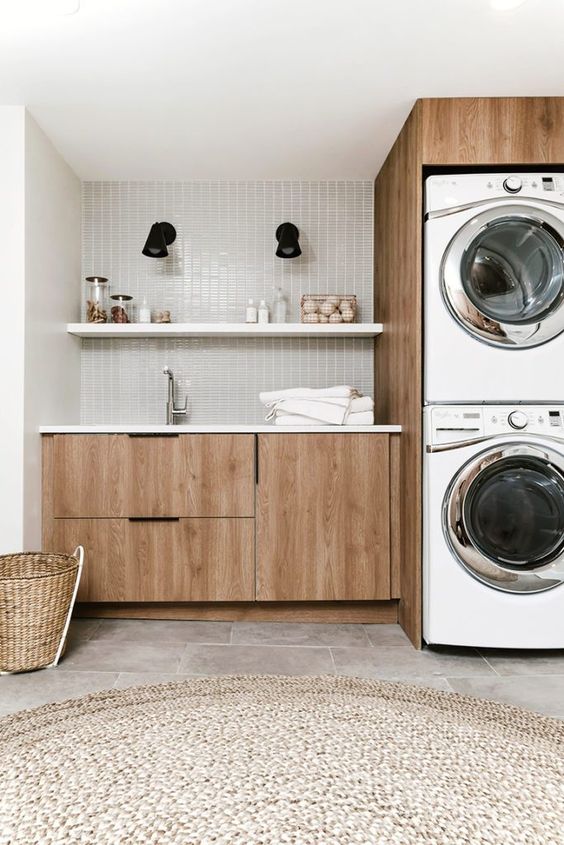 a mid century modern laundry with sleek stained cabinets, a grey skinny tile backsplash, a jute rug and stacked appliances