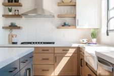 a modern farmhouse kitchen with light-stained cabinets, a navy kitchen island, white stone countertops and a skinny tile backsplash, black handles
