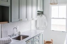 a modern farmhouse laundry with green shaker style cabinets, a penny tile backsplash, a grey and white tile floor