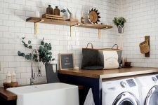 a modern farmhouse laundry with navy cabinets, wooden countertops and open shelving, potted greenery and baskets