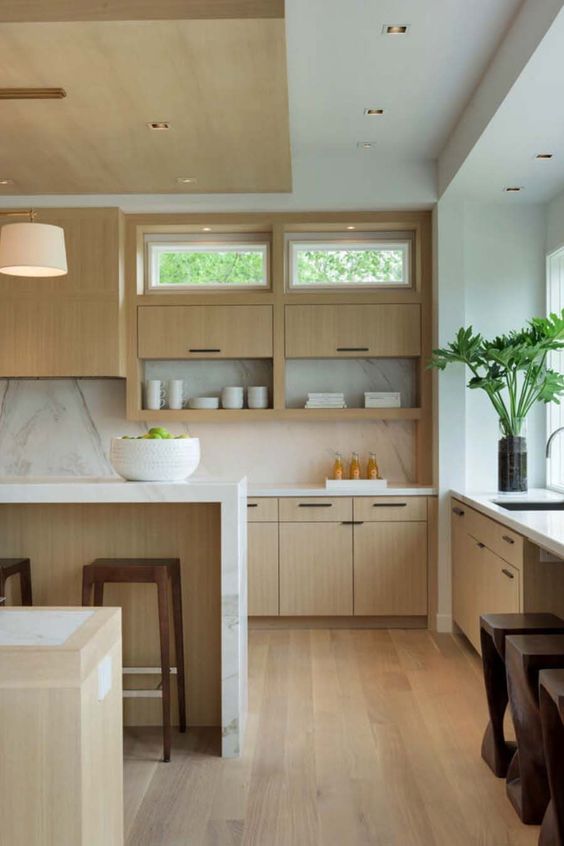 a modern light-stained kitchen with a white marble backsplash and countertops, simple lamps and windows here and there