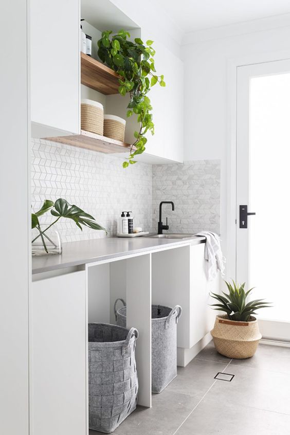 a modern neutral laundry with sleek white cabinets, a marble tile backsplash with a geo print and felt baskets for storage