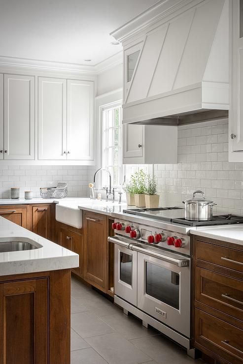 a modern two-tone kitchen with white upper and stained lower cabinets, white stone countertops, a metal hood painted white is great
