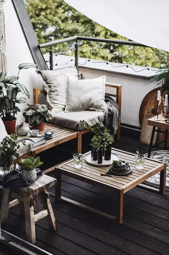 a monochromatic balcony with a black floor, natural wooden furniture, neutral textiles, potted greenery and candles