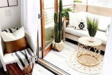 a neutral boho balcony with a white sofa, potted cacti and greenery, a rattan table, a jute rug and printed pillows
